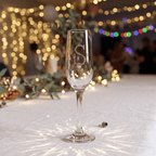 Champagne flute with 'S' logo on a festive background with lights and decorations.