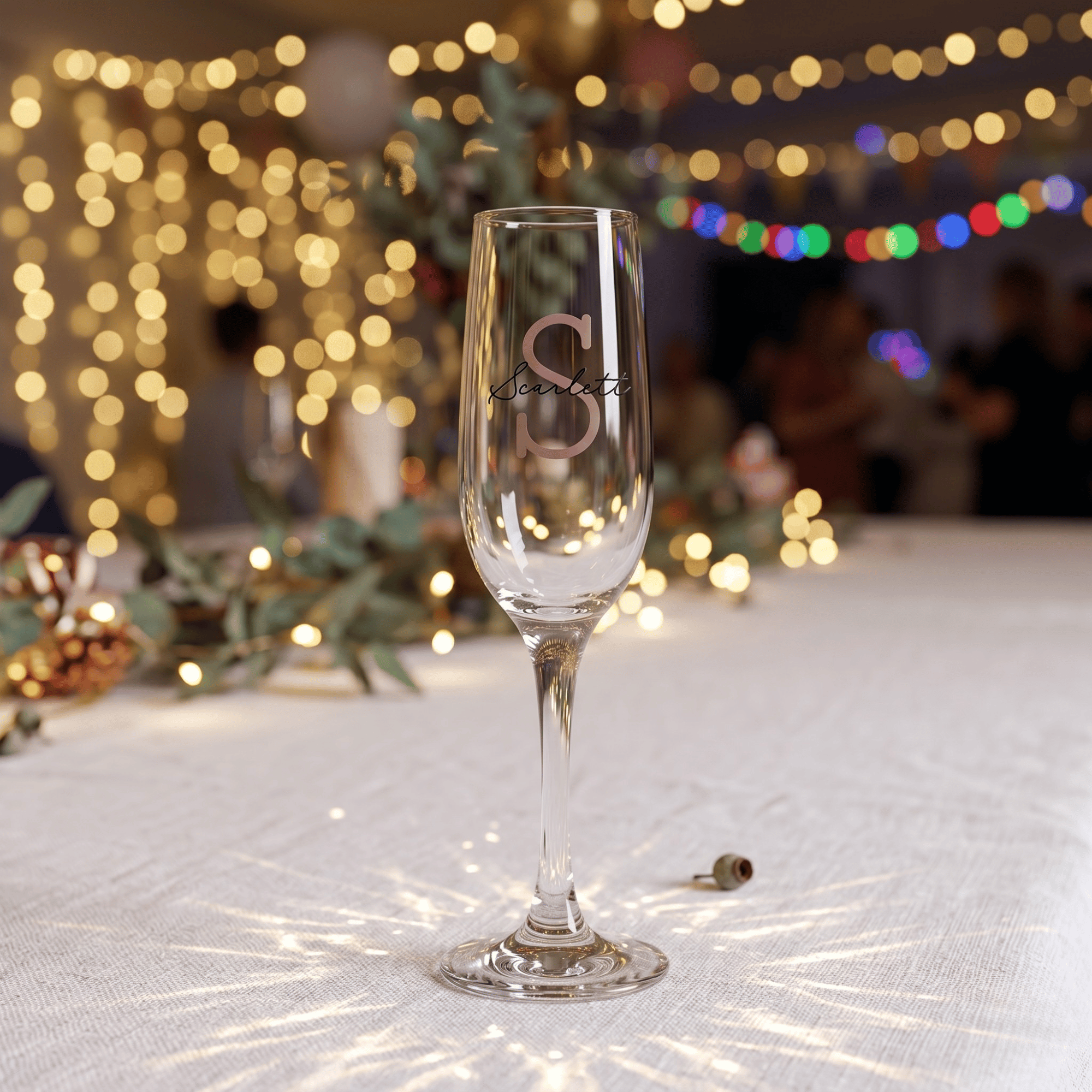 Champagne flute with 'S' logo on a festive background with lights and decorations.