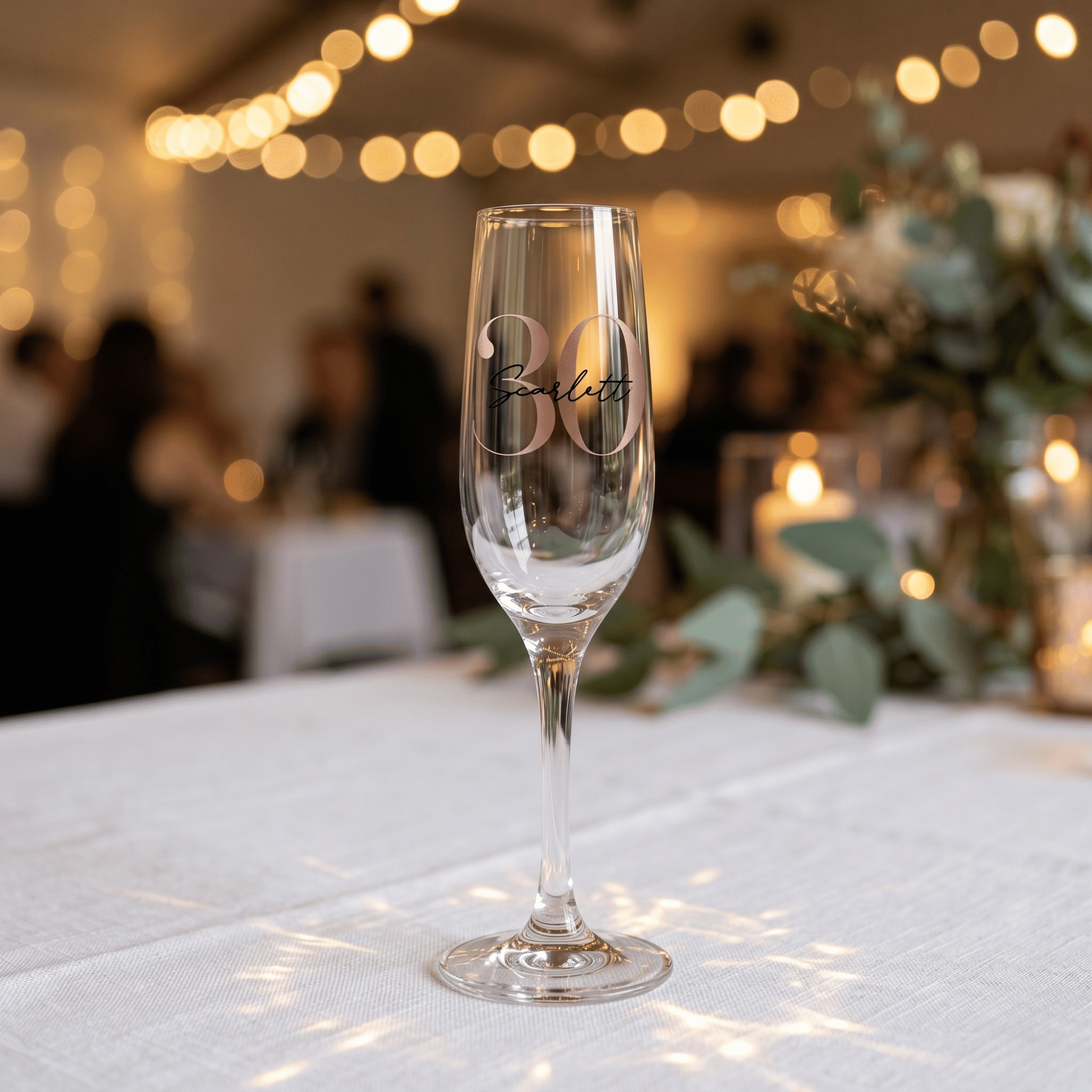 Champagne flute with '30' engraving on a tablecloth with blurred festive background