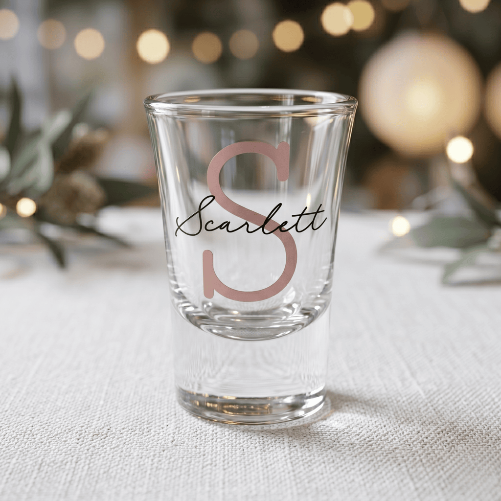 Clear shot glass with 'Scarlett' engraving on a textured surface with blurred lights in the background