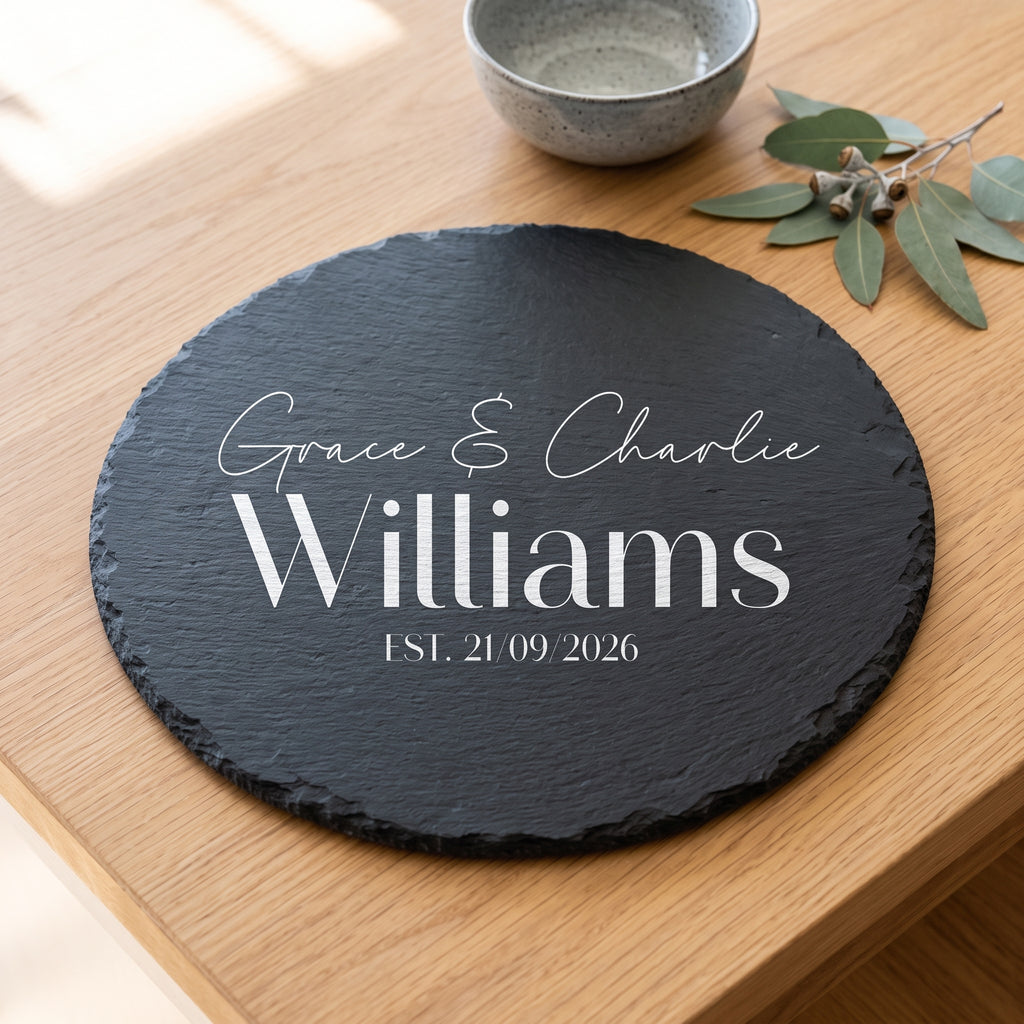 A round black slate coaster with personalised white text reading 'Grace & Charlie Williams EST. 21.09.2026