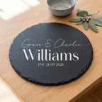 A round black slate coaster with personalised white text reading 'Grace & Charlie Williams EST. 21.09.2026