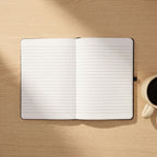 Custom laser engraved corporate notebook in black vegan leather with a metallic pen, displayed on an executive timber desk in a bright office.