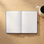 Custom laser engraved corporate notebook in black vegan leather with a metallic pen, displayed on an executive timber desk in a bright office.