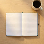 Custom laser engraved corporate notebook in black vegan leather with a metallic pen, displayed on an executive timber desk in a bright office.