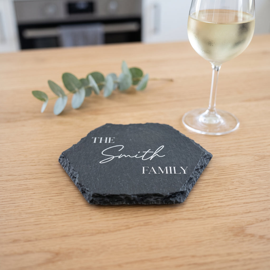 Close up of custom laser engraving on a dark geometric slate coaster showing traditional classic lettering and chipped edges.