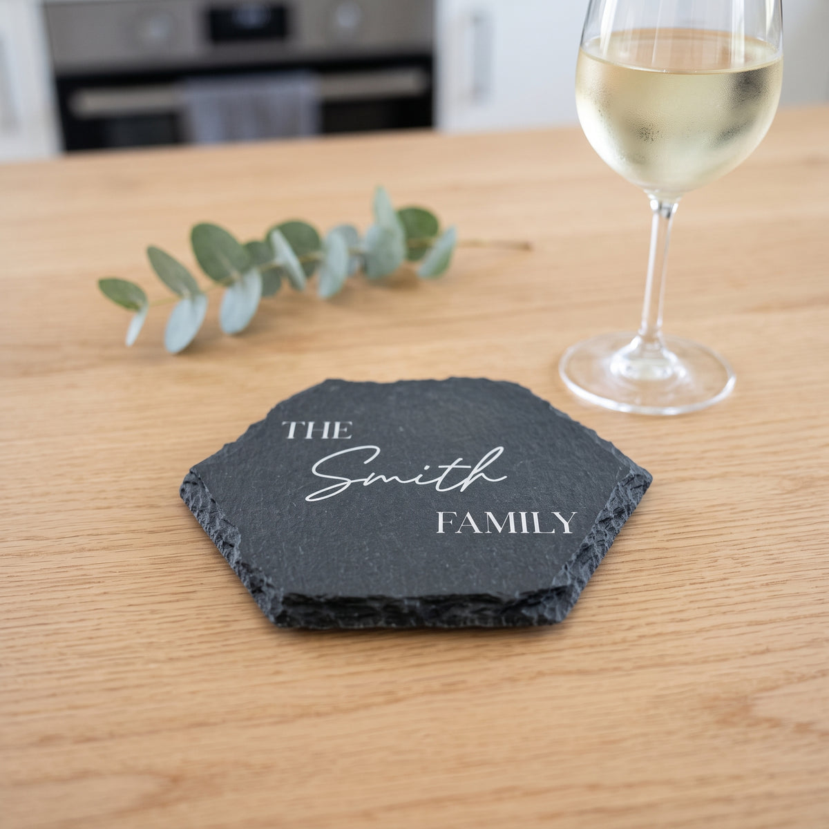 Close up of custom laser engraving on a dark geometric slate coaster showing traditional classic lettering and chipped edges.