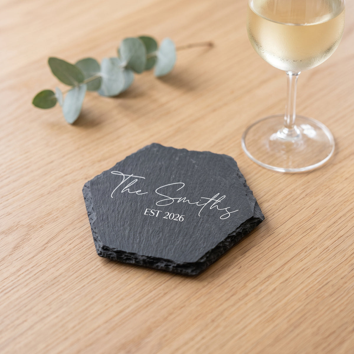 Close up of custom laser engraving on a dark geometric slate coaster showing clean contemporary lettering and chipped edges.