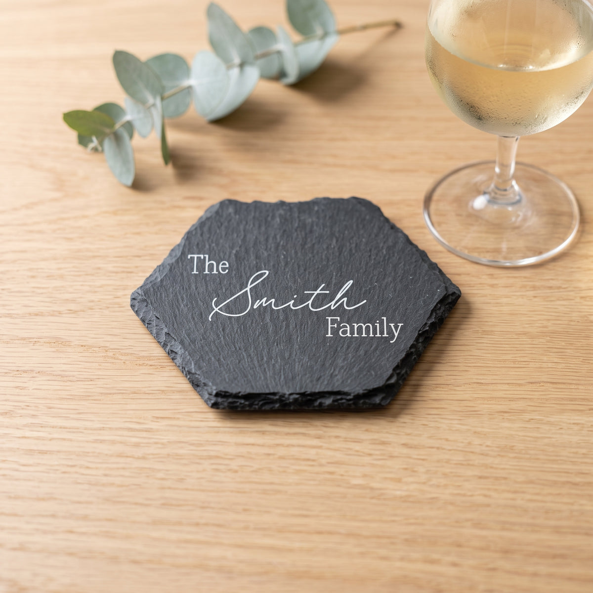 Close up of custom laser engraving on a dark geometric slate coaster showing traditional balanced lettering and chipped edges.