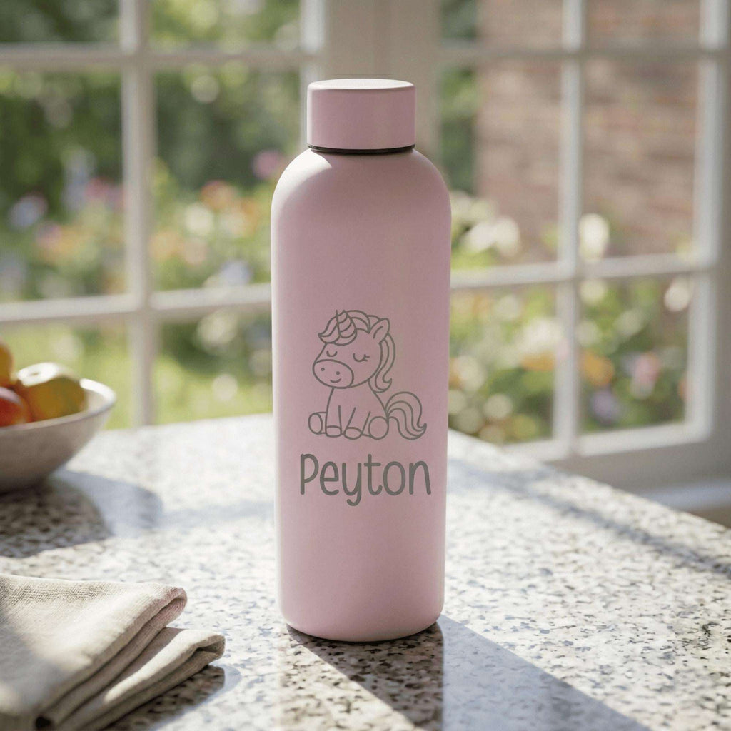 Pink water bottle with unicorn design and 'Peyton' text on a table with a blurred garden background