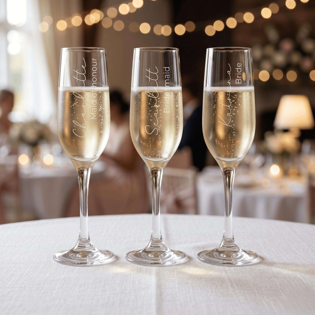 Three champagne glasses with personalised inscriptions on a table with blurred background
