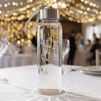 Personalised "Ruby Bride" glass water bottle with a silver lid, serving as an elegant bridal gift or wedding day accessory at a beautifully decorated reception table.