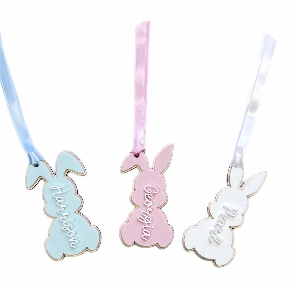 Set of three personalised Easter bunny tags in pastel blue, pink, and white – names "Harrison", "Georgia", and "Pearl" in script font with satin ribbons.