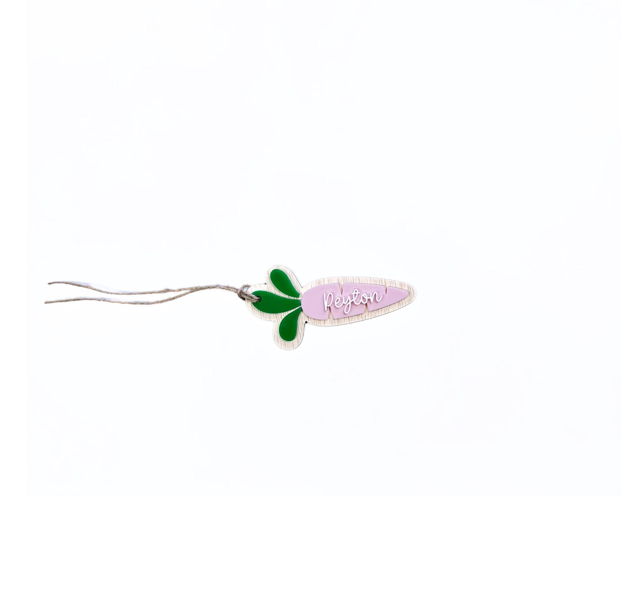Pink acrylic carrot-shaped Easter name tag with white "Peyton" script – personalised Easter basket tag with green leaves and twine.