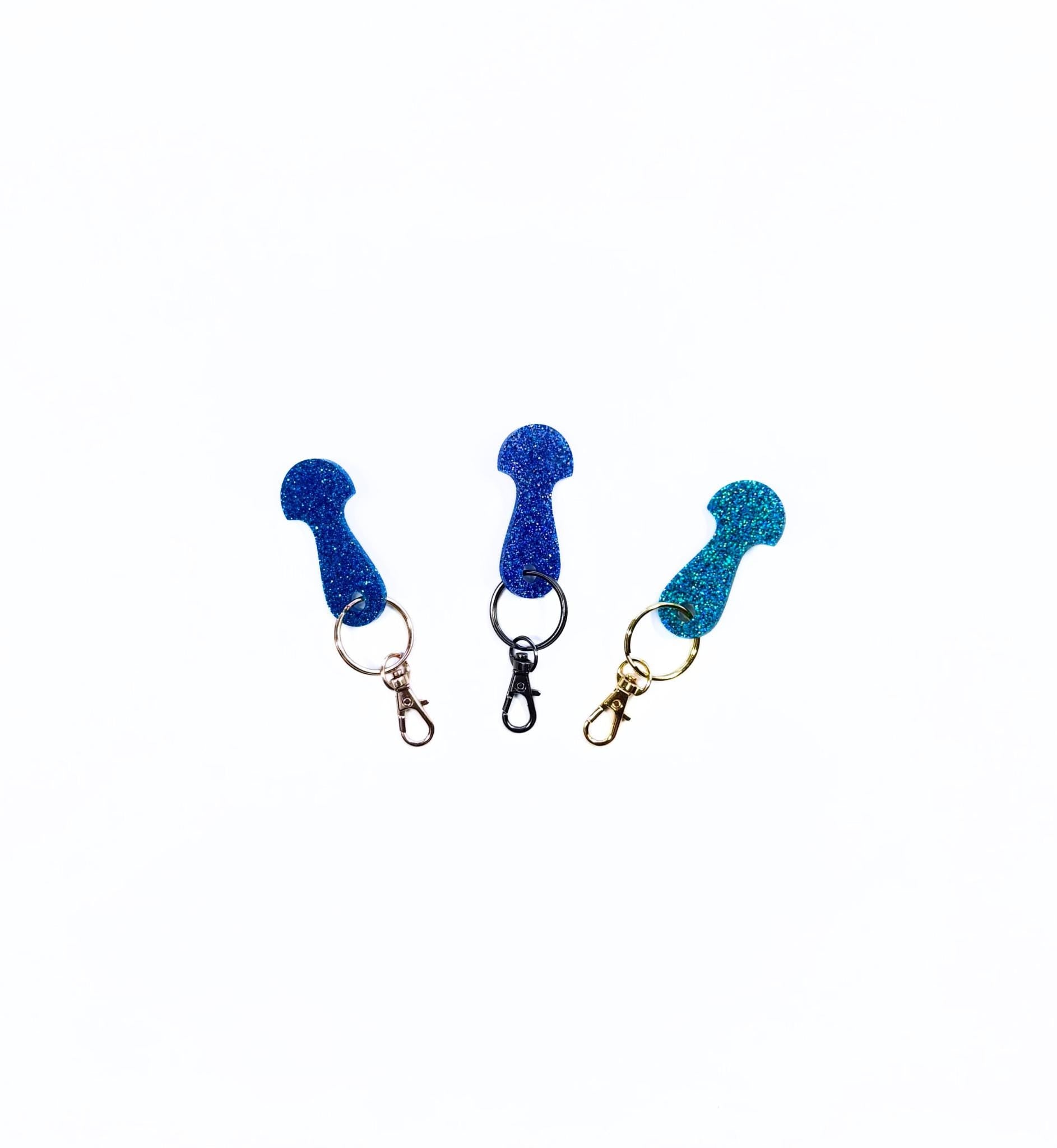 Three glitter acrylic trolley token keychains in red, pink, and purple with different hardware styles including rose gold, silver, and black.