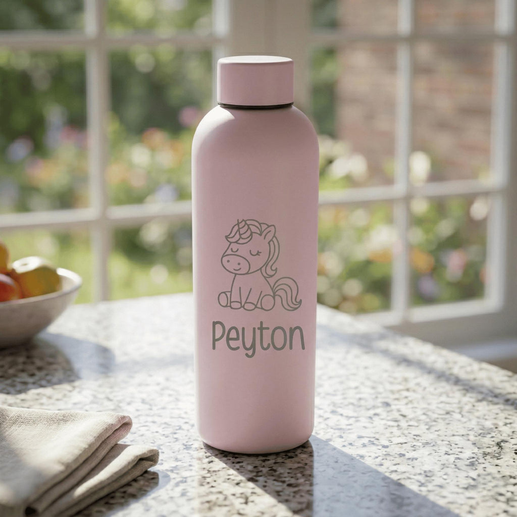 Pink water bottle with unicorn design and 'Peyton' text on a table with a blurred garden background