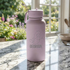 Pink water bottle with mermaid design and 'Georgia' text on a marble surface with garden view
