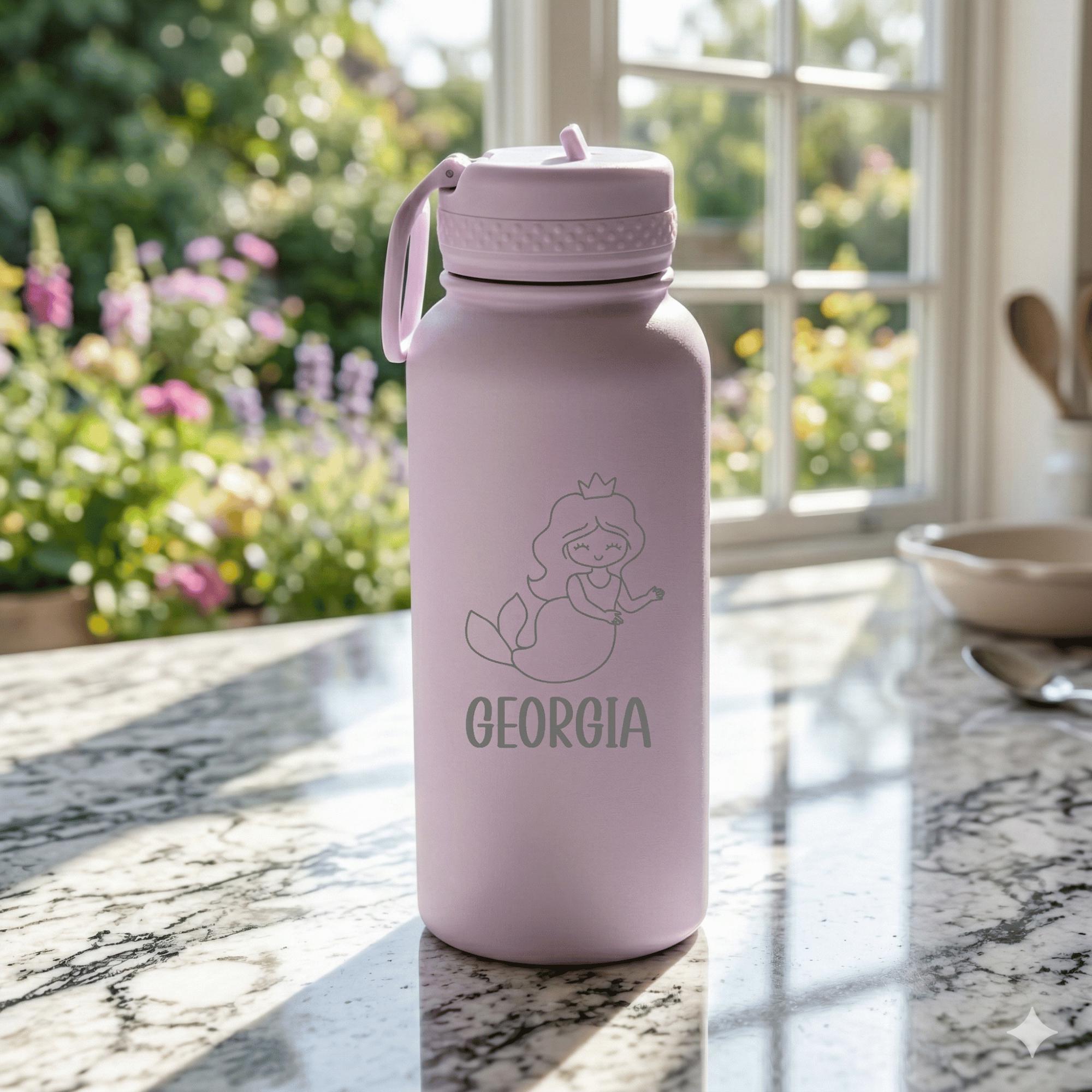 Pink water bottle with mermaid design and 'Georgia' text on a marble surface with garden view