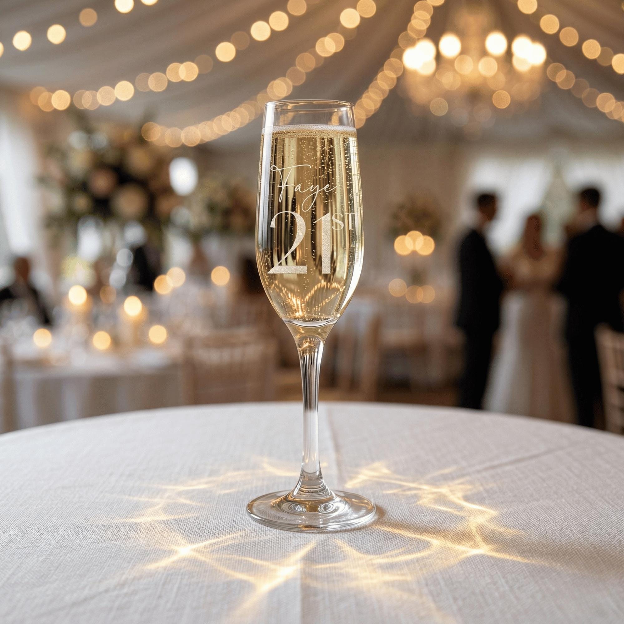 Champagne flute with 'Happy 21st' engraving on a tablecloth with blurred festive background