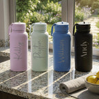 Four insulated water bottles with names engraved on them, placed on a kitchen counter.