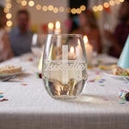 Personalized glass on a festive table with blurred people and lights in the background