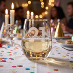 Glass of white wine with '21' and a name on it, set against a festive background with candles and confetti.