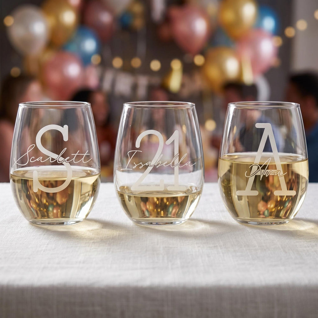Three personalized wine glasses with names on a table with balloons and people in the background
