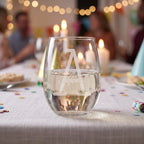 Glass of water with a logo on a table with people and lights in the background