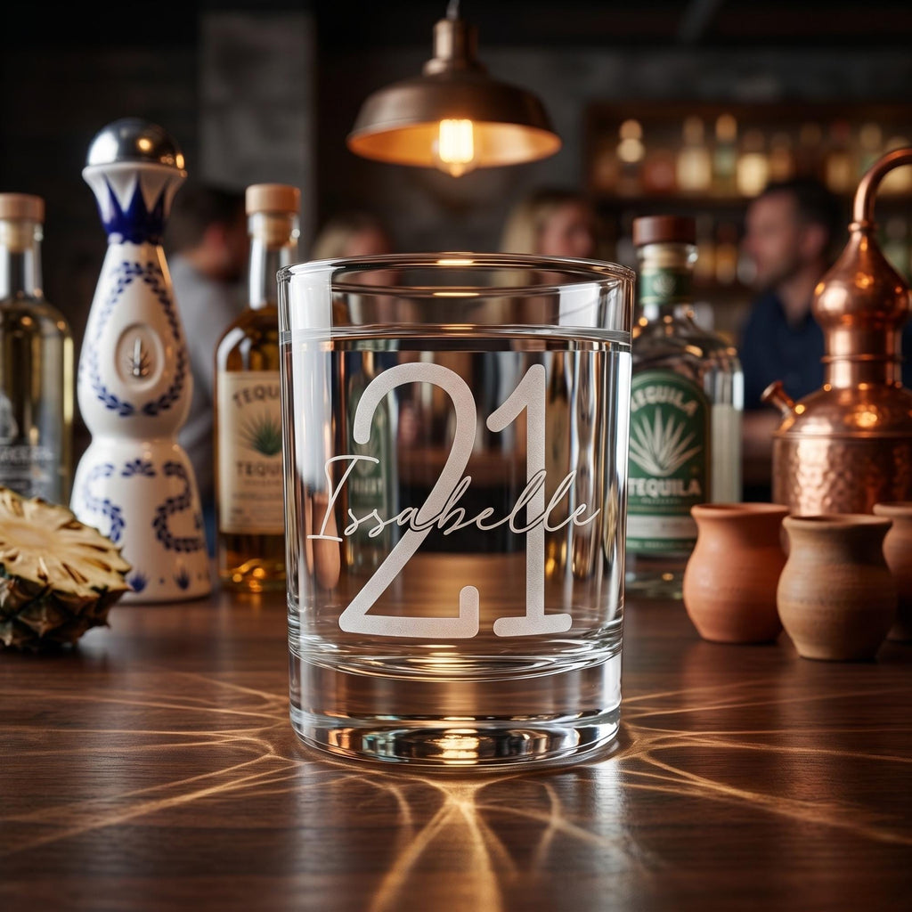 Clear glass with '21 Isabelle' engraving on a bar counter with tequila bottles in the background
