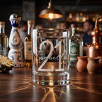 Clear glass with '21 Isabelle' engraving on a bar counter with tequila bottles in the background