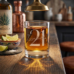 Glass of tequila with '21 Issabella' engraving on a wooden bar with tequila bottle and lime garnish.