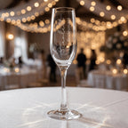 Personalised bridesmaid gift champagne flute with "Scarlett Bridesmaid" engraving, displayed on a table at a wedding celebration with elegant string lights.