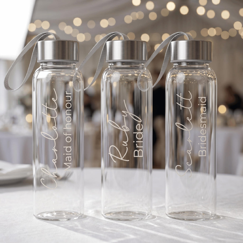 Three personalised glass water bottles for a bridal party featuring "Charlotte Maid of honour", "Ruby Bride", and "Scarlett Bridesmaid" in elegant white script, displayed at a wedding reception.