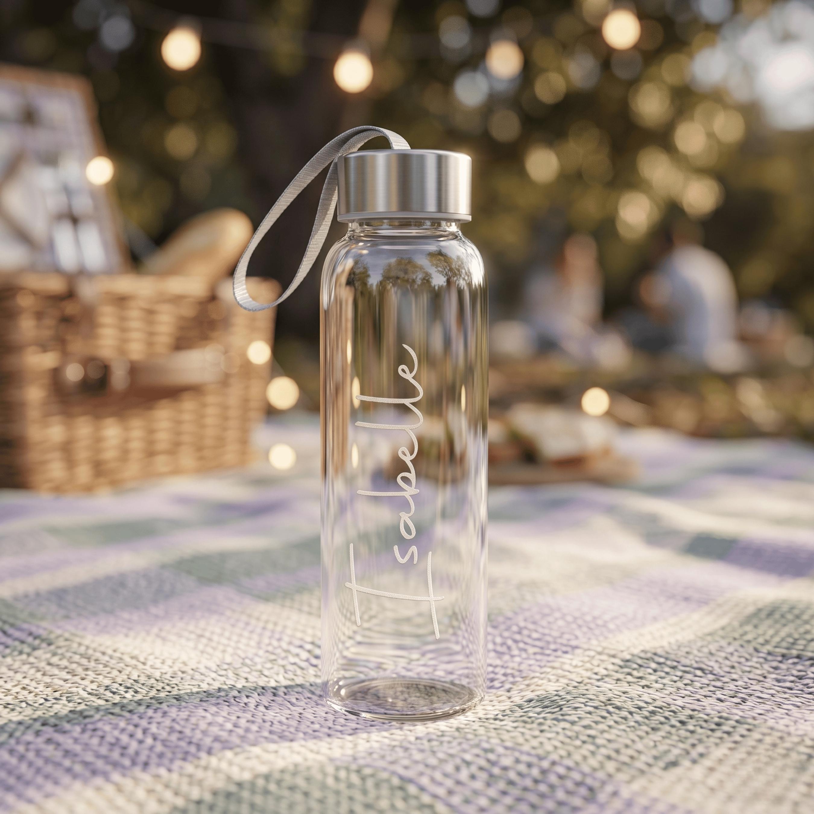Personalised glass water bottle for Isabelle, displayed on a picnic rug next to a wicker basket and warm outdoor garden lights.