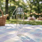 Custom engraved glass bottle with the name "Scarlett" and a silver carry strap, pictured on a blue and white picnic rug in a leafy Australian park.