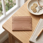Personalised tan vegan leather card holder with the name "Scarlett" in Gold  Script font, resting on a wooden desk next to Australian coins and keys.