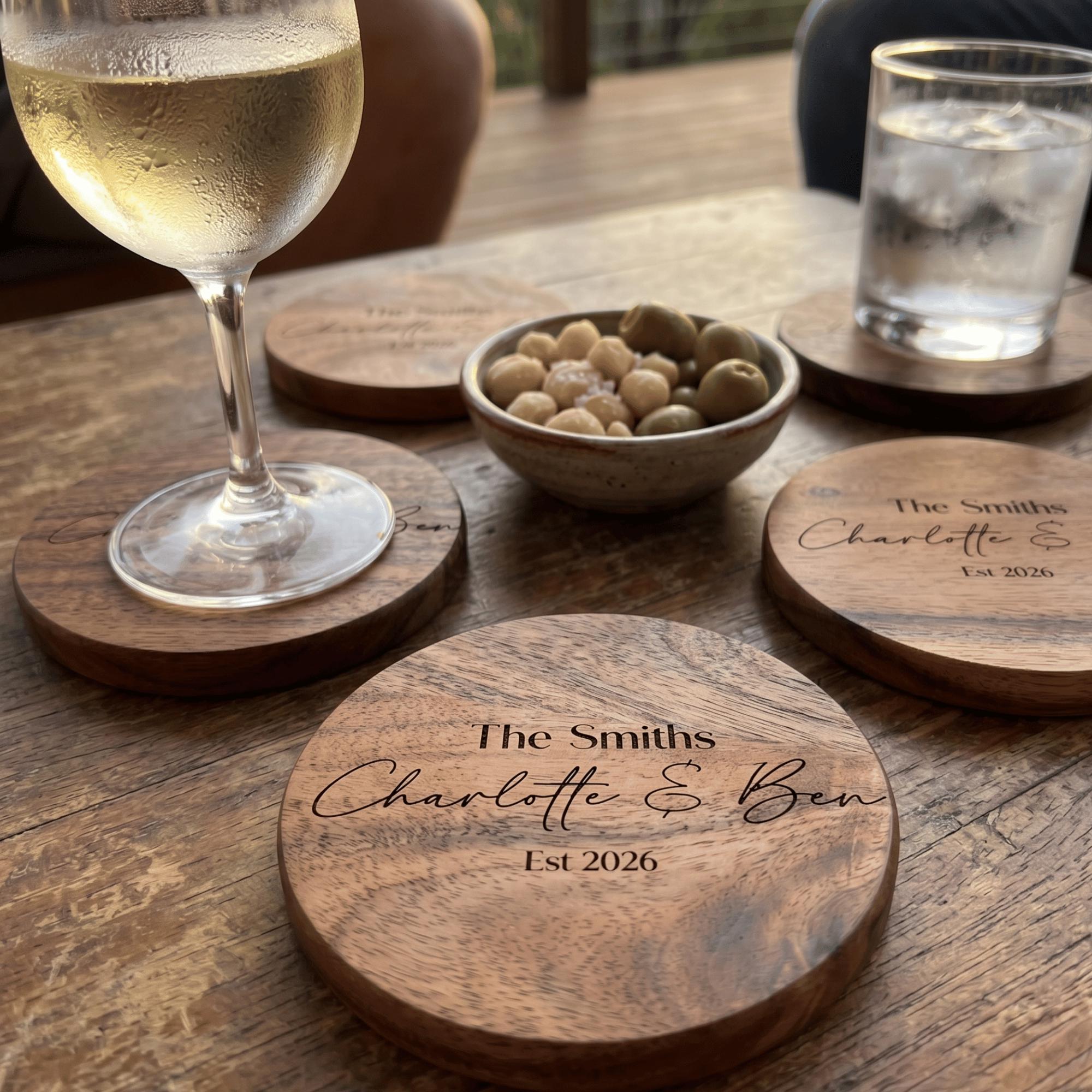 Wooden coasters with engraved names on a wooden table with drinks.