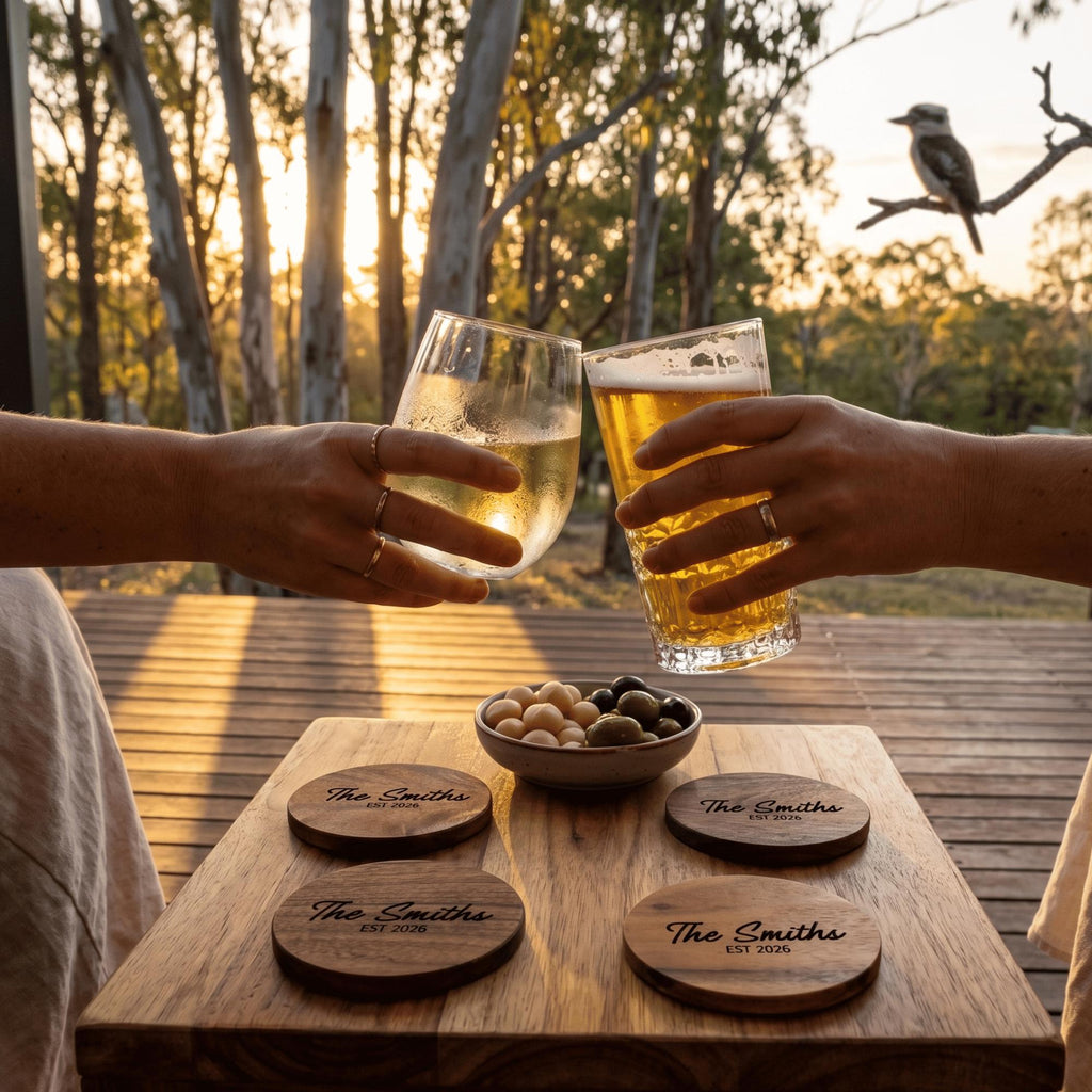 Two people toasting with glasses of beer on a wooden table outdoors during sunset.