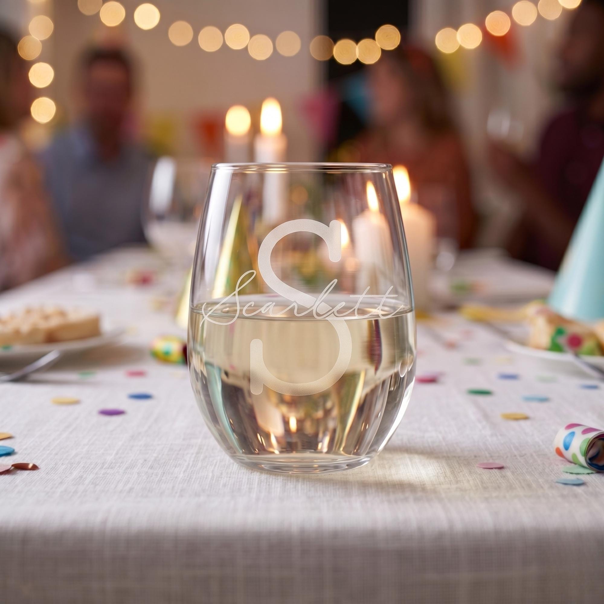 Personalized stemless wine glass on a table with blurred people and lights in the background