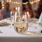 Glass with '30' on a table with people and decorations in the background