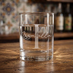 Clear glass with 'Issabella' engraving on a wooden surface with blurred bottles in the background