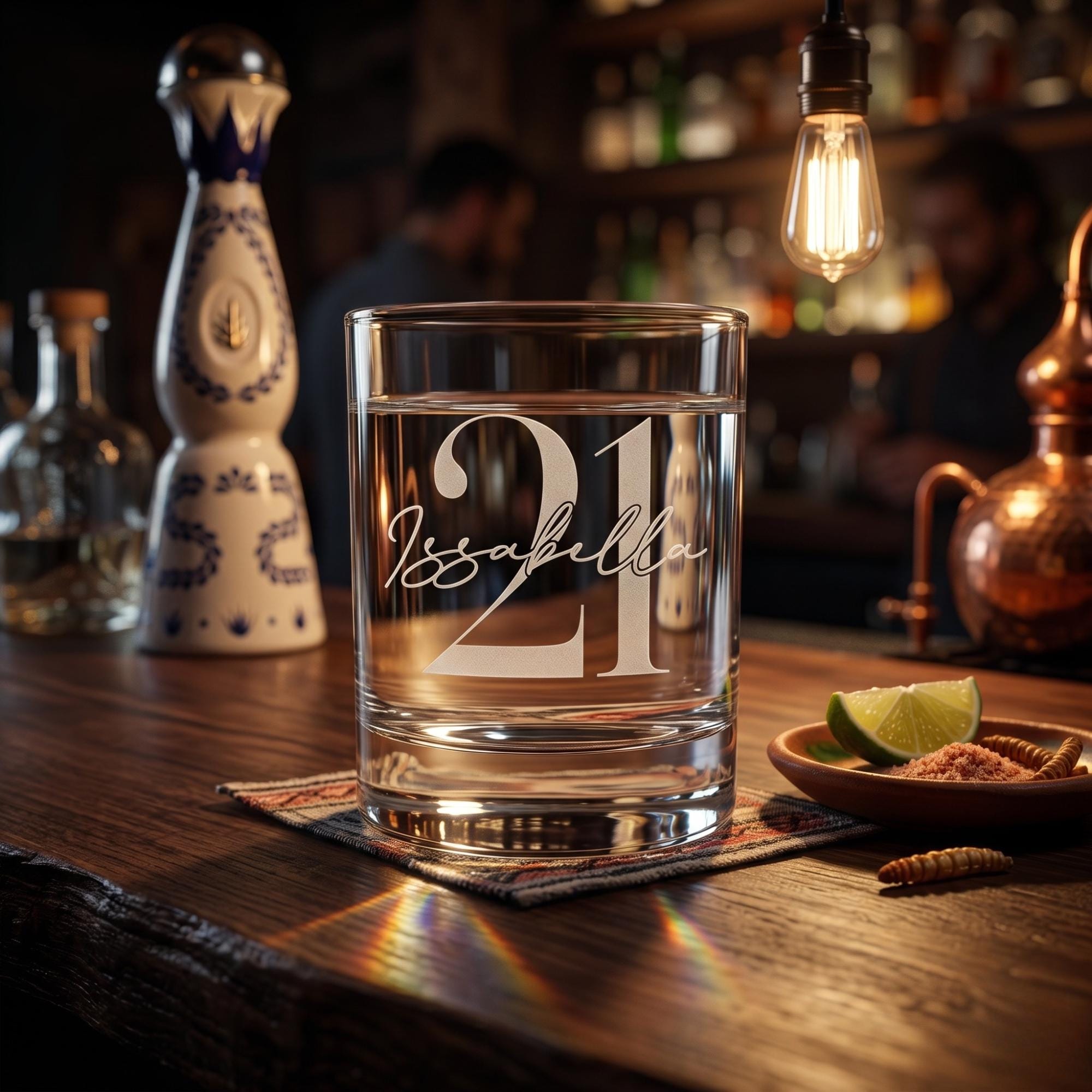 Glass with '21 Isabella' engraving on a bar counter with bottles and lime in the background