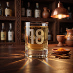 Glass of whiskey with '18 Scarlett' engraving on a wooden bar counter with bottles and decor in the background.