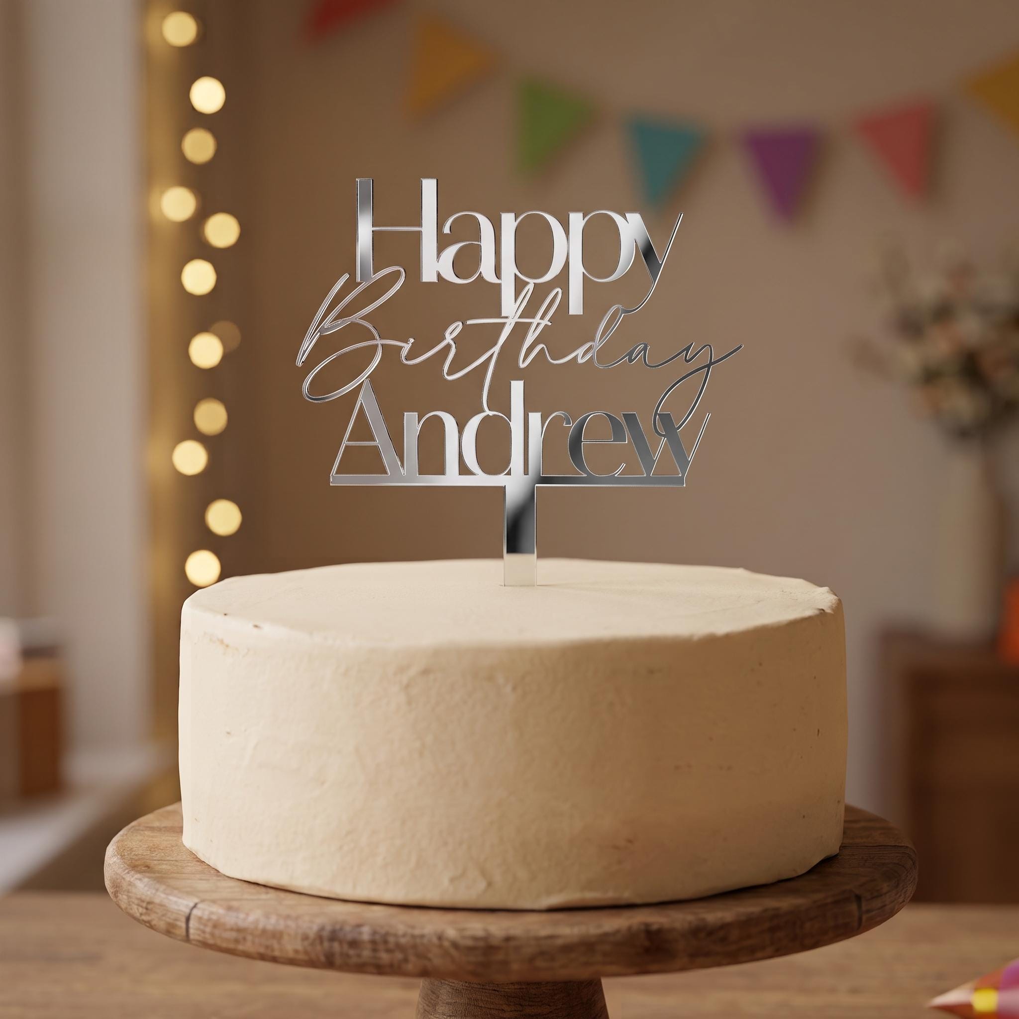 Custom Happy Birthday Andrew silver mirror acrylic cake topper placed on an iced cake.