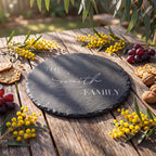 Personalised round slate cheese board engraved with THE Smith FAMILY in all caps serif and delicate script font on timber table.