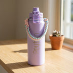 Lilac insulated 1.1L drink bottle with pastel paracord handle showing the custom laser engraved name Peyton on a sunlit wooden bench.