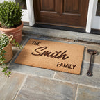 Personalised coir doormat measuring 40 by 60cm featuring custom family surname lettering on a stone doorstep.