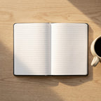 Personalised hardcover lined notebook in blue with custom metallic hot foil monogram lettering, displayed on a wooden desk with coffee.