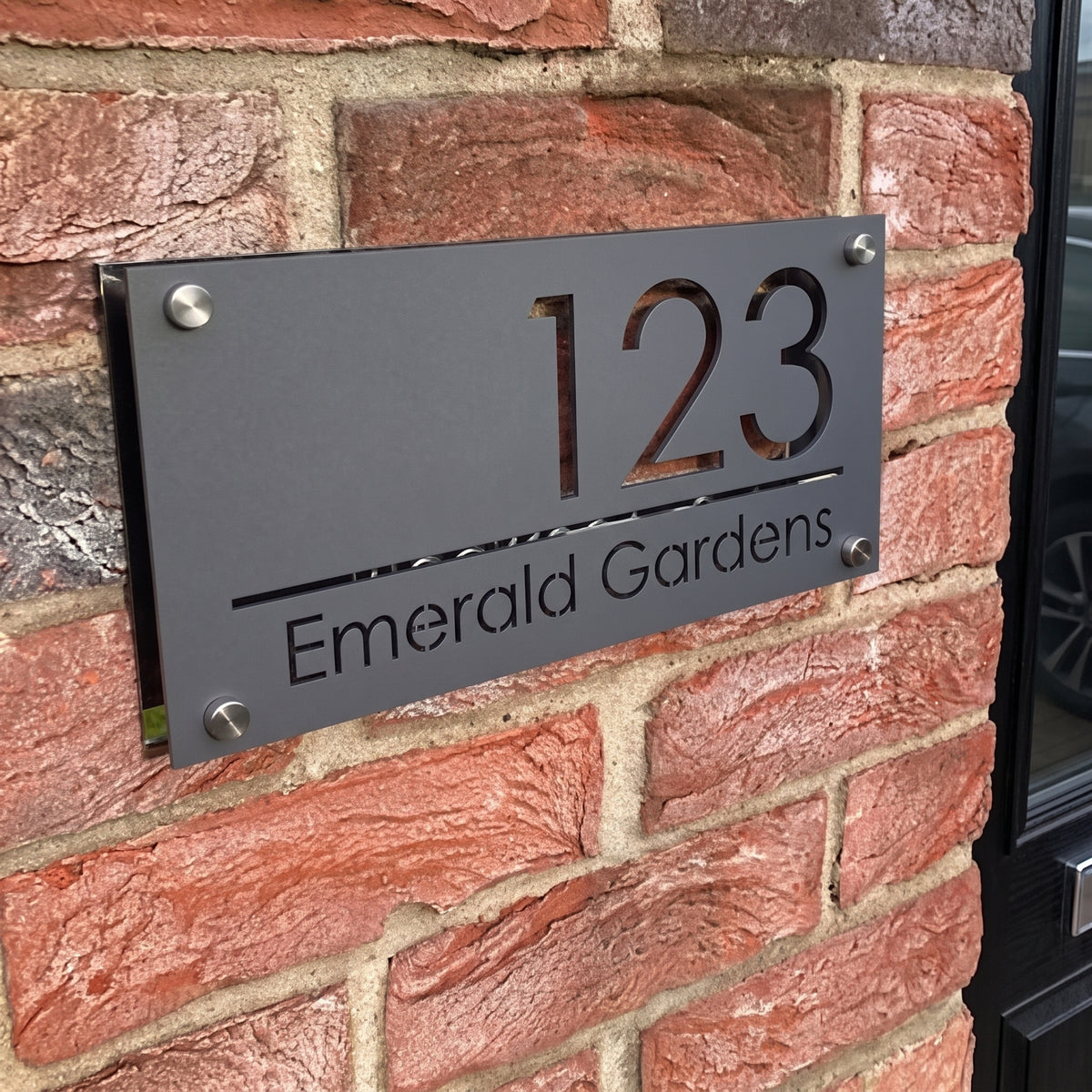 Personalised matt black acrylic door sign with white laser cut house number and street name mounted with silver metal stand offs.