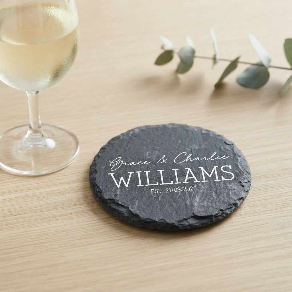 Personalised round slate coaster laser engraved in Timeless Classic font layout on natural dark stone surface.